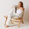 Woman sitting on a wooden chair wearing colorful pajama pants and a beige cardigan.