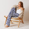 Woman sitting on a wooden chair wearing a white tank top, beige cardigan, and blue patterned pants.