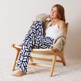 Woman sitting on a wooden chair wearing a white tank top, beige cardigan, and blue patterned pants.