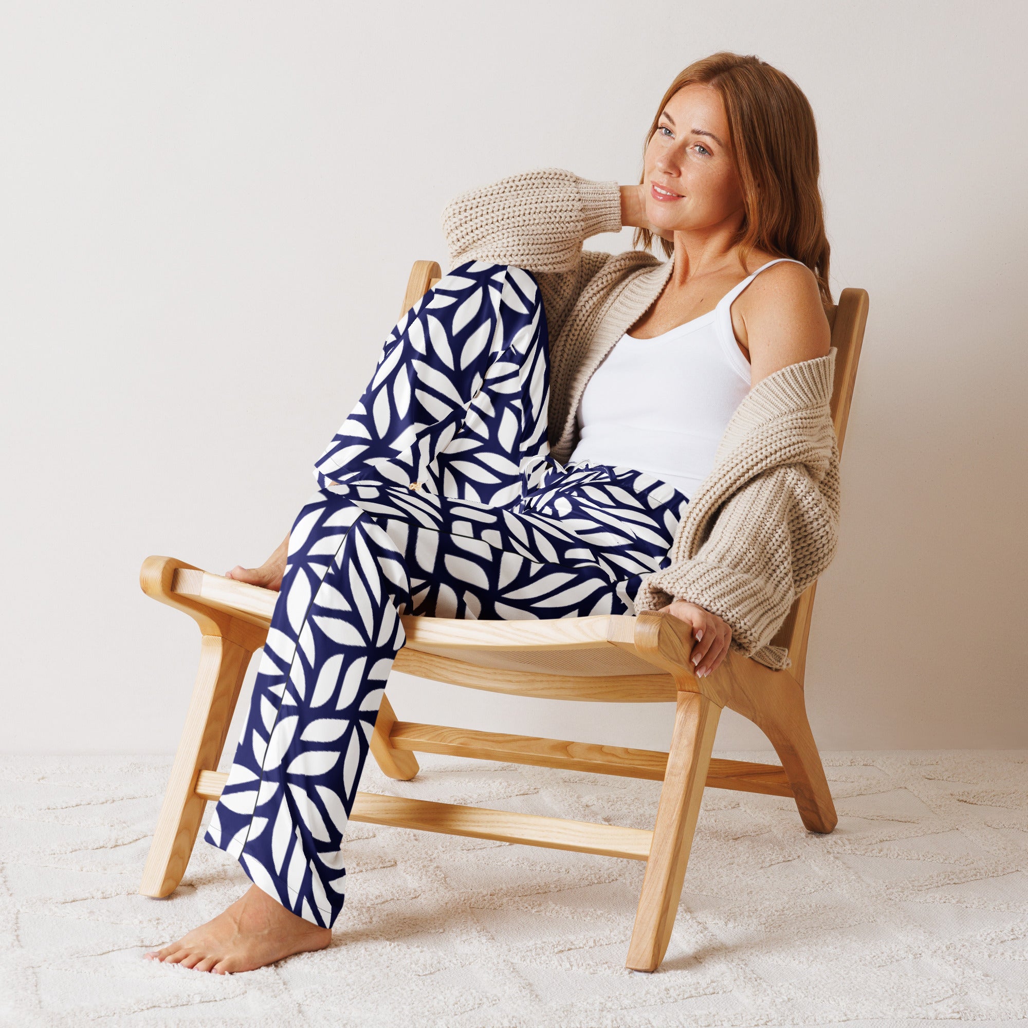 Woman sitting on a wooden chair wearing a white tank top, beige cardigan, and blue patterned pants.
