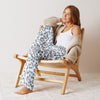 Woman sitting on a wooden chair wearing blue checkered pajama pants and a beige cardigan.