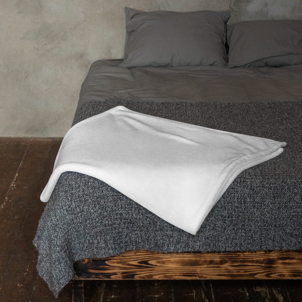 Gray textured bedspread with a white blanket on a wooden bed frame against a concrete wall.