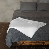 Gray textured bedspread with a white blanket on a wooden bed frame against a concrete wall.