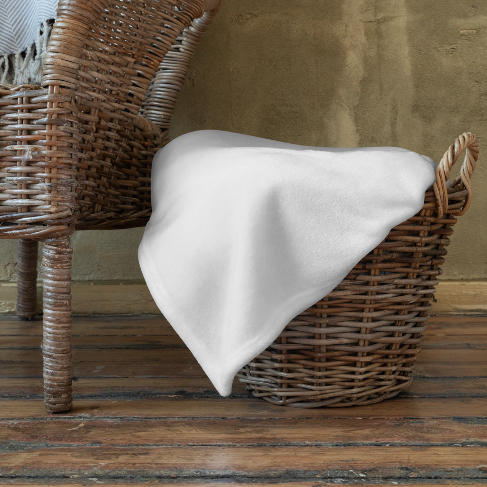 White blanket draped over a wicker basket on a wooden floor with a textured wall background