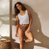Woman wearing a white tank top and patterned shorts standing against a beige wall.