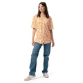 Woman wearing a patterned orange and white shirt and blue jeans on a white background