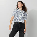 Woman wearing a white t-shirt with blue floral pattern and black jeans on a light gray background