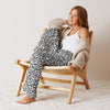 Woman sitting on a wooden chair wearing a patterned outfit and beige cardigan.