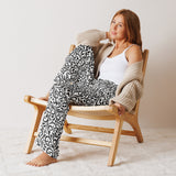 Woman sitting on a wooden chair wearing a patterned outfit and beige cardigan.