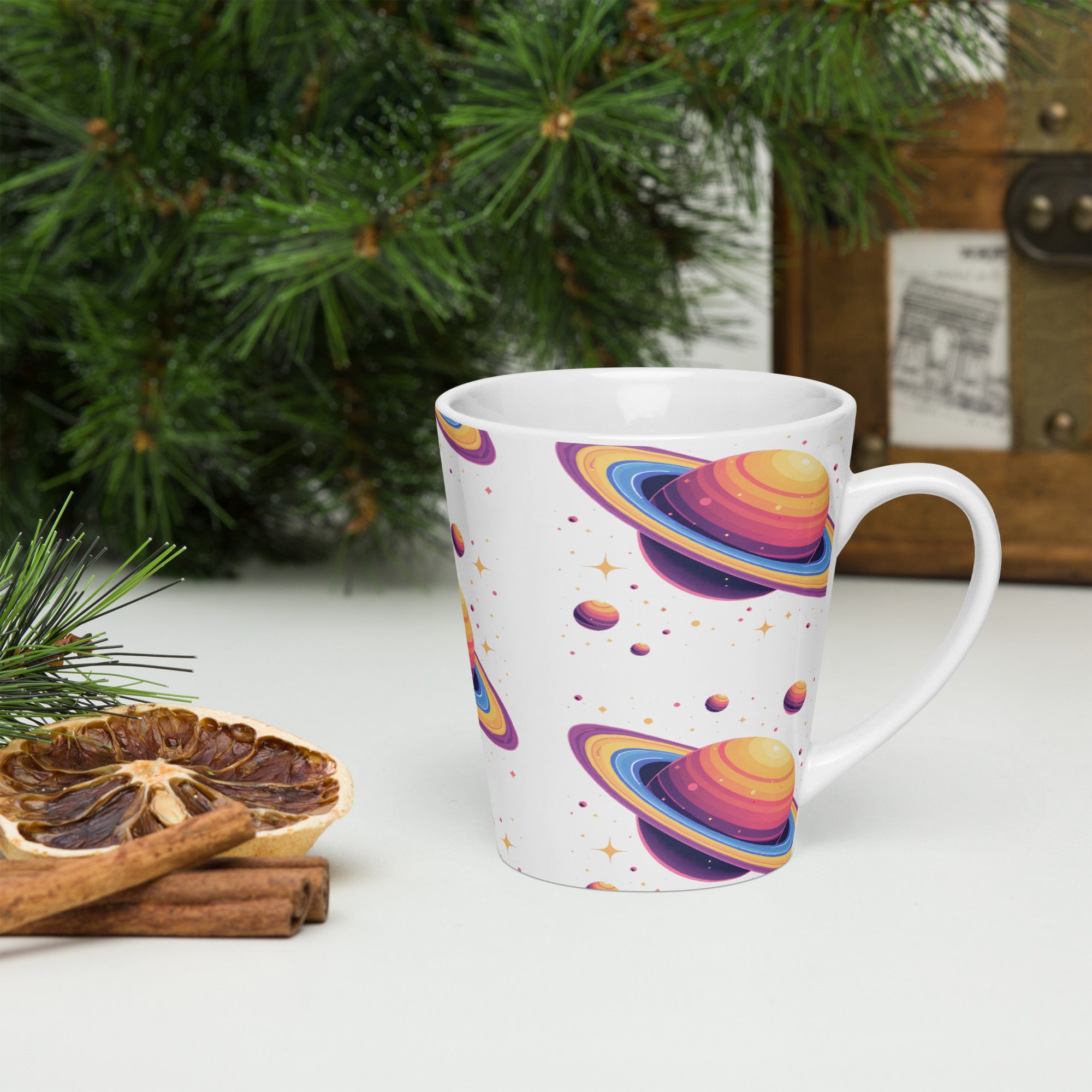 White mug with colorful planet design on a white surface with Christmas decorations.