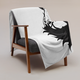 White blanket with black dragon design draped over a wooden chair on a beige background